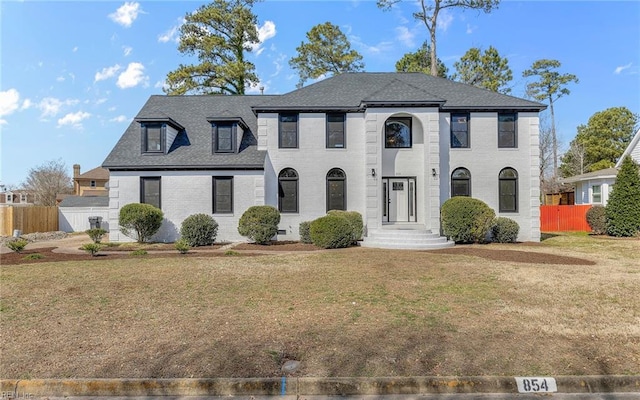 view of front of property featuring a shingled roof, a front yard, brick siding, and fence