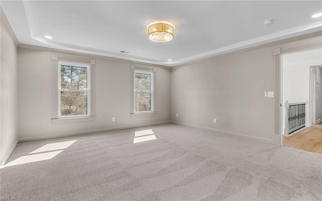 empty room featuring ornamental molding, a tray ceiling, light carpet, and baseboards