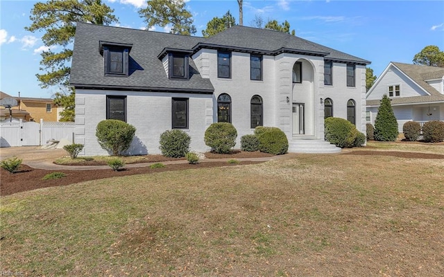 view of front of house featuring brick siding, fence, roof with shingles, a gate, and a front yard