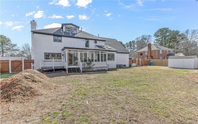 back of house with a shed, a lawn, a fenced backyard, and a sunroom