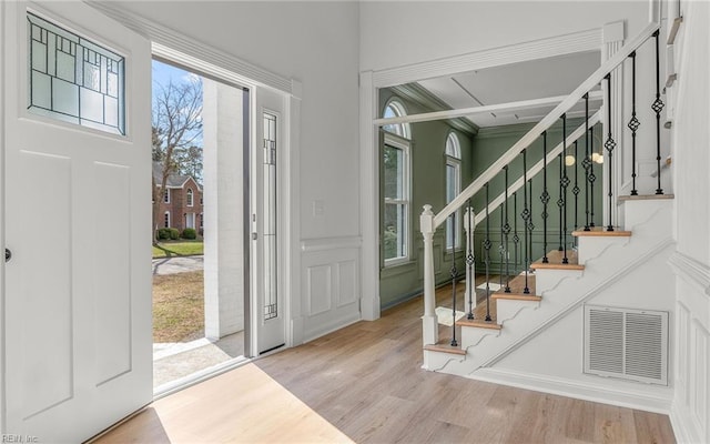 foyer entrance featuring stairs, wood finished floors, visible vents, and a decorative wall