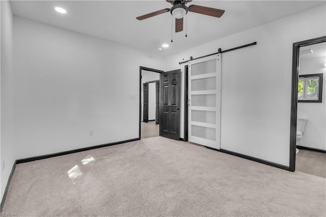 unfurnished bedroom featuring a barn door, recessed lighting, baseboards, carpet, and ensuite bath