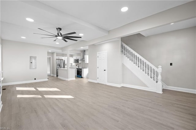 unfurnished living room with stairway, light wood-style floors, a ceiling fan, electric panel, and baseboards