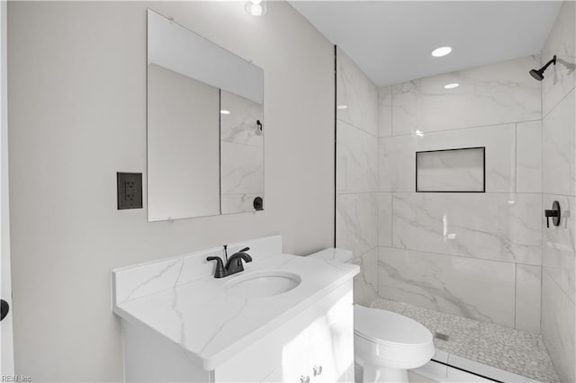 bathroom featuring toilet, recessed lighting, a tile shower, and vanity