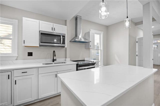 kitchen featuring stainless steel appliances, a healthy amount of sunlight, a sink, and wall chimney range hood