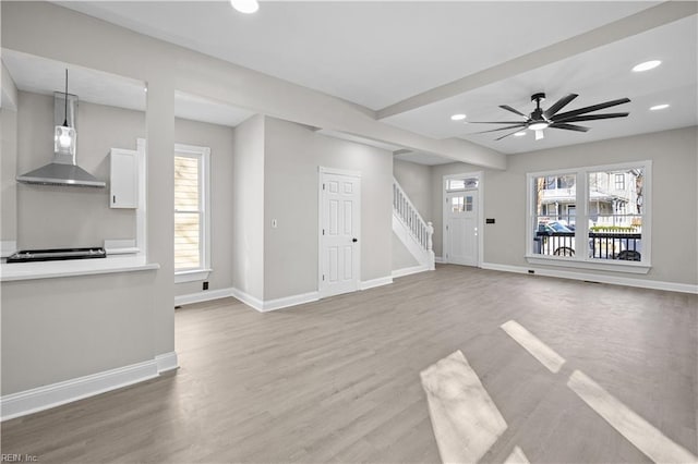 unfurnished living room with baseboards, stairway, wood finished floors, a healthy amount of sunlight, and recessed lighting