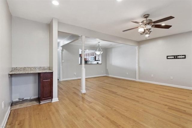 basement featuring ceiling fan, light wood finished floors, and baseboards