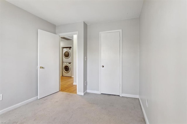 unfurnished bedroom featuring baseboards, carpet, and stacked washer / drying machine