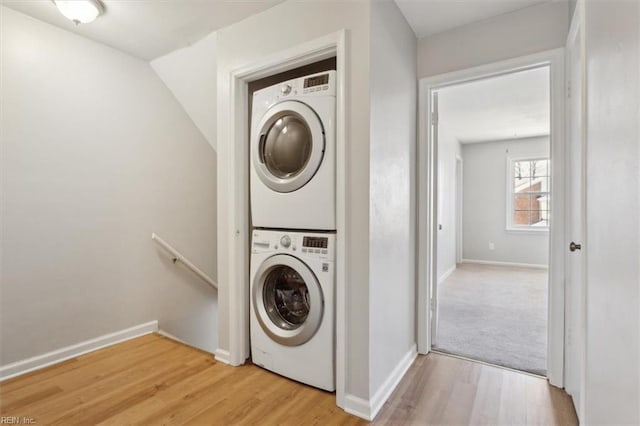 laundry room featuring baseboards, laundry area, stacked washer and clothes dryer, and light wood-style floors