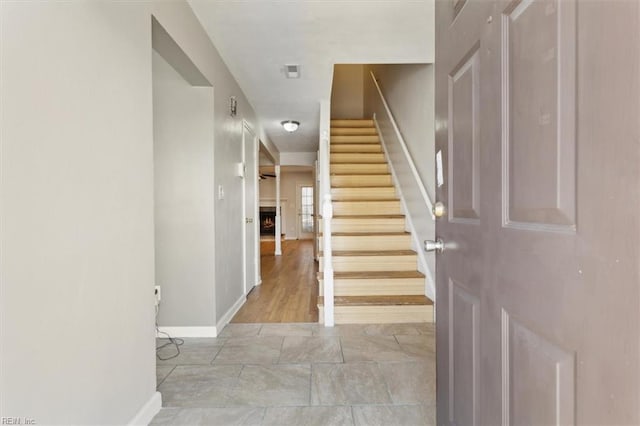 entryway featuring stairs, a warm lit fireplace, and baseboards