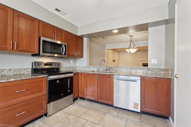 kitchen with brown cabinets, visible vents, appliances with stainless steel finishes, a sink, and light stone countertops