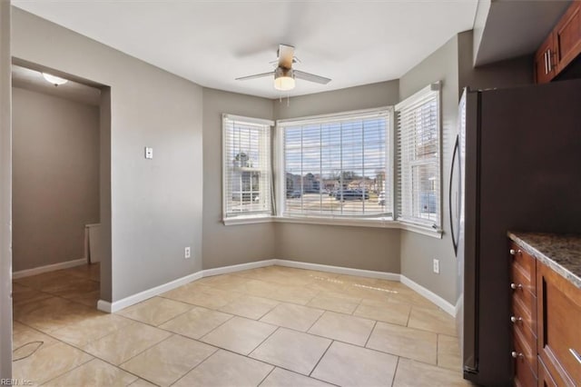 unfurnished dining area featuring light tile patterned floors, a ceiling fan, and baseboards