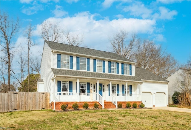 colonial home featuring a porch, a front yard, fence, and driveway