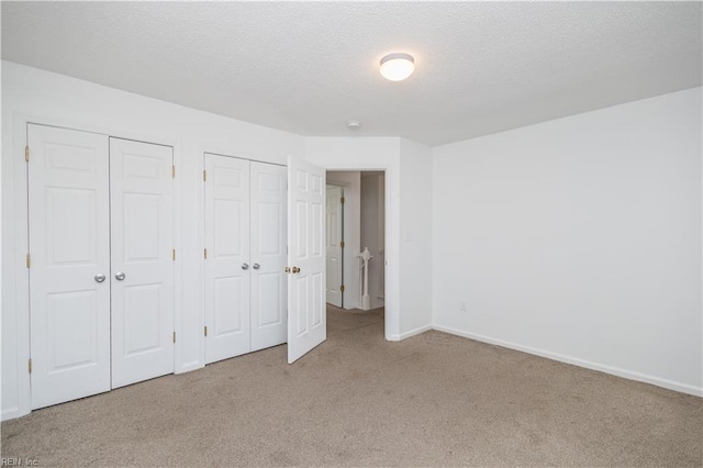 unfurnished bedroom featuring a textured ceiling, carpet floors, two closets, and baseboards