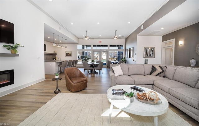 living area with wood finished floors, ornamental molding, a glass covered fireplace, and a ceiling fan