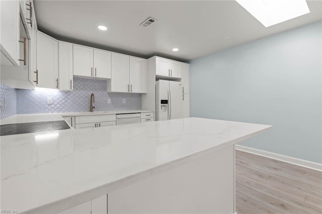 kitchen with white appliances, a skylight, a sink, light wood-type flooring, and tasteful backsplash