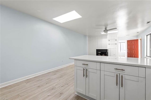 kitchen featuring a skylight, baseboards, light countertops, light wood-type flooring, and white cabinetry