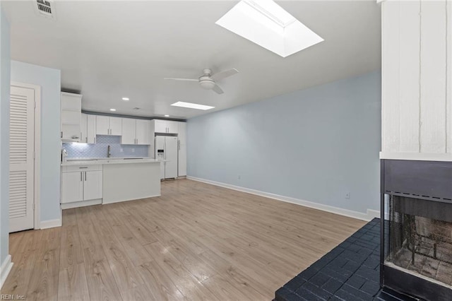 living room featuring a skylight, baseboards, visible vents, a ceiling fan, and light wood-style floors