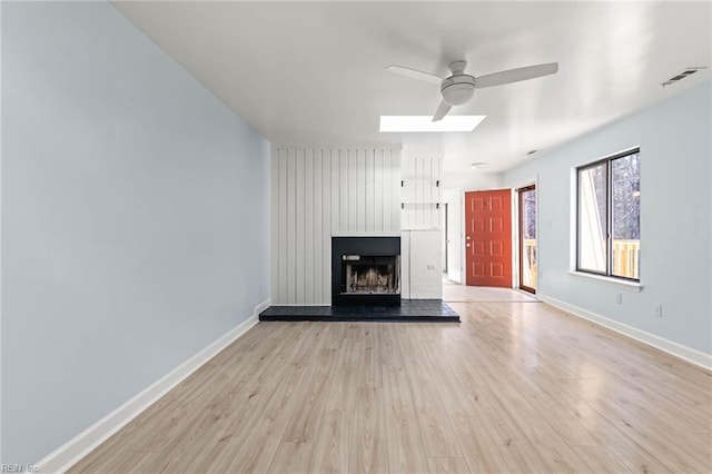 unfurnished living room with a fireplace with raised hearth, a ceiling fan, visible vents, baseboards, and light wood-type flooring