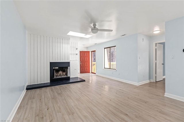 unfurnished living room with light wood-style floors, a fireplace with raised hearth, ceiling fan, and baseboards