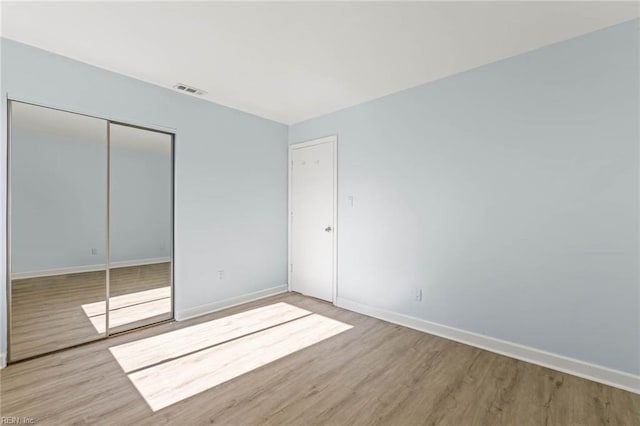 unfurnished bedroom featuring a closet, wood finished floors, visible vents, and baseboards