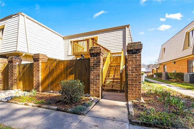 view of front of property featuring central AC, brick siding, stairway, and fence