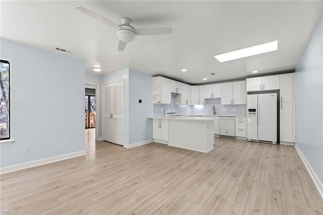 kitchen with a skylight, visible vents, decorative backsplash, white appliances, and a peninsula