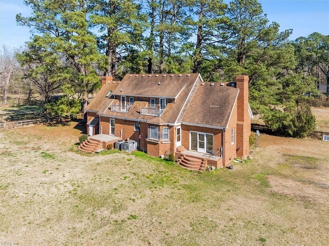 back of house featuring central AC unit, a balcony, brick siding, a yard, and a chimney