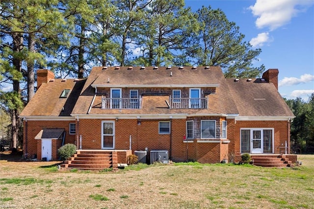 rear view of house featuring a balcony, brick siding, a chimney, and a yard