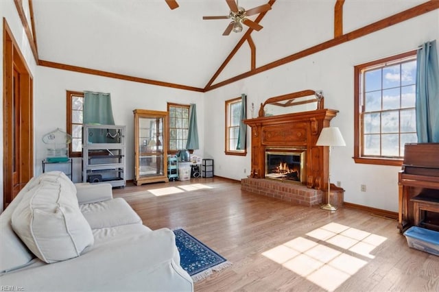 living area featuring baseboards, a ceiling fan, wood finished floors, a brick fireplace, and high vaulted ceiling