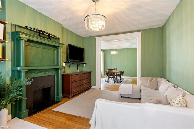 living area with an inviting chandelier, a fireplace with flush hearth, baseboards, and wood finished floors