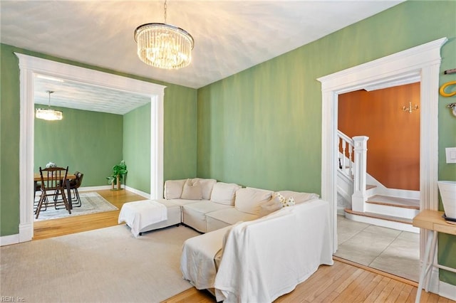 living room featuring stairs, baseboards, wood finished floors, and a notable chandelier