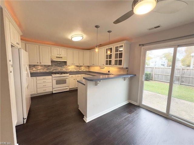 kitchen featuring white appliances, visible vents, dark countertops, a peninsula, and under cabinet range hood