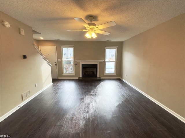 unfurnished living room featuring a fireplace with raised hearth, dark wood-style flooring, a ceiling fan, visible vents, and baseboards