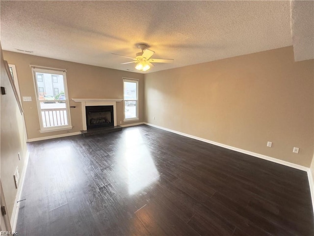 unfurnished living room featuring baseboards, a fireplace with raised hearth, dark wood-style floors, ceiling fan, and a textured ceiling