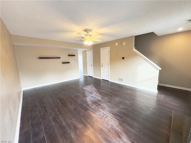 unfurnished living room featuring a textured ceiling, ceiling fan, dark wood-type flooring, visible vents, and baseboards