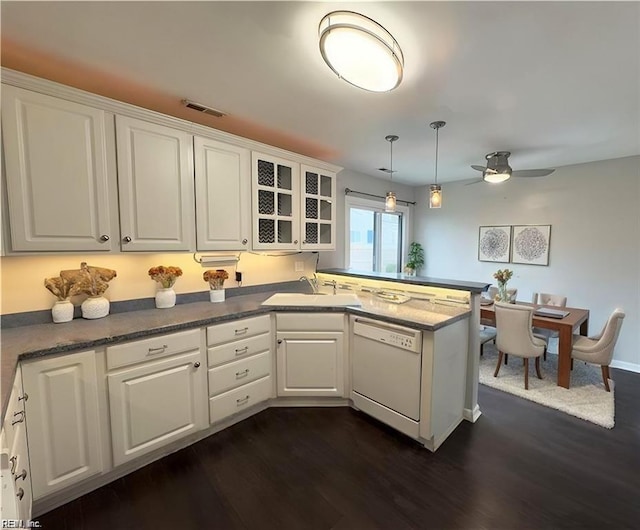 kitchen featuring white dishwasher, a peninsula, a sink, white cabinets, and dark wood finished floors