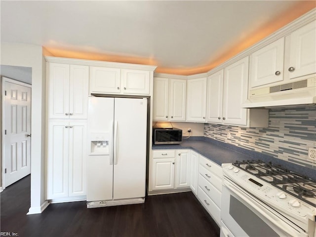 kitchen featuring white appliances, white cabinets, dark countertops, dark wood-style floors, and under cabinet range hood