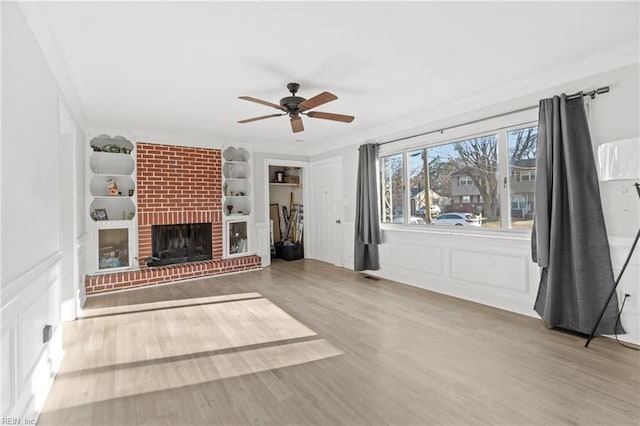 unfurnished living room with a decorative wall, wood finished floors, built in features, ornamental molding, and a brick fireplace