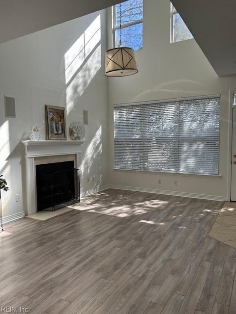 unfurnished living room with wood finished floors, a fireplace with flush hearth, a high ceiling, and baseboards