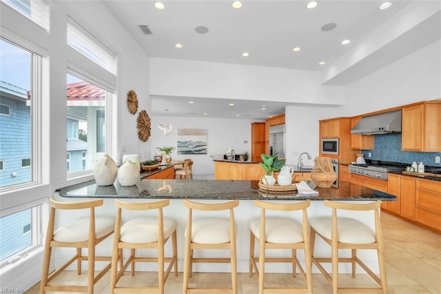 kitchen with tasteful backsplash, visible vents, dark stone counters, wall chimney exhaust hood, and built in appliances