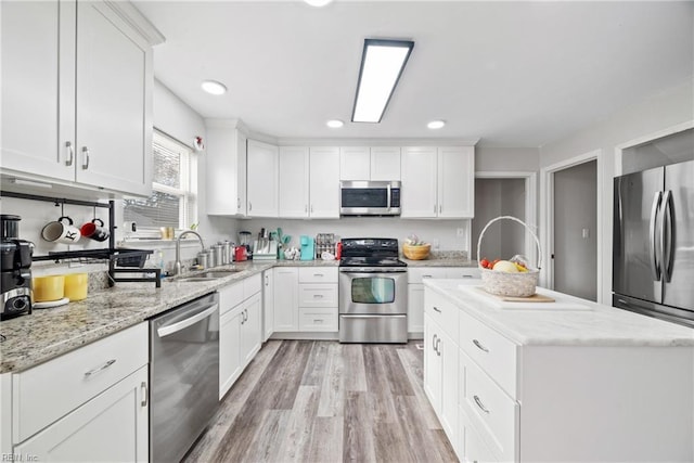 kitchen with white cabinets, a center island, stainless steel appliances, light wood-type flooring, and a sink