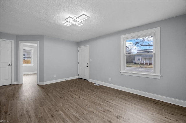 spare room with a textured ceiling, wood finished floors, and baseboards