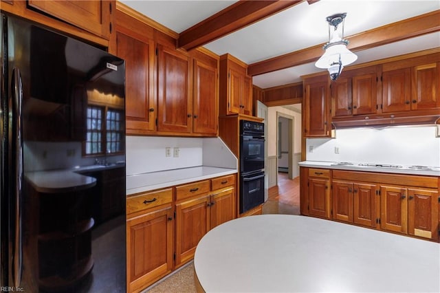 kitchen with pendant lighting, beam ceiling, light countertops, under cabinet range hood, and black appliances