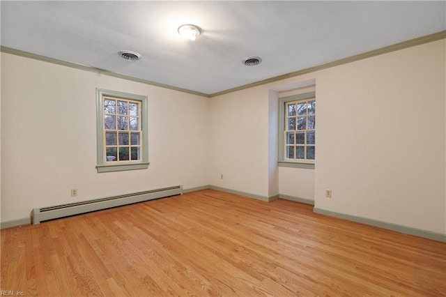 spare room with visible vents, ornamental molding, baseboard heating, light wood-type flooring, and a wealth of natural light
