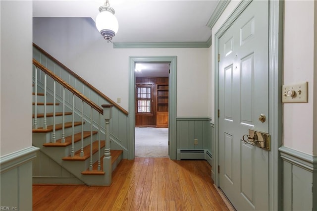 interior space featuring a decorative wall, wood finished floors, ornamental molding, baseboard heating, and wainscoting
