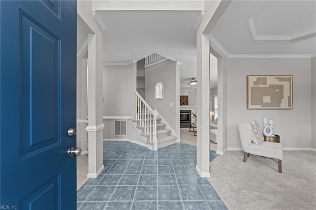 tiled entryway featuring visible vents, a glass covered fireplace, ornamental molding, carpet, and stairs