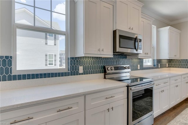 kitchen featuring stainless steel appliances, ornamental molding, white cabinetry, and decorative backsplash