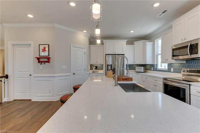 kitchen with appliances with stainless steel finishes, white cabinets, a sink, and ornamental molding