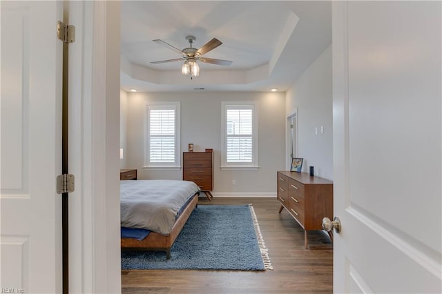 bedroom with a ceiling fan, baseboards, a tray ceiling, and dark wood-style flooring